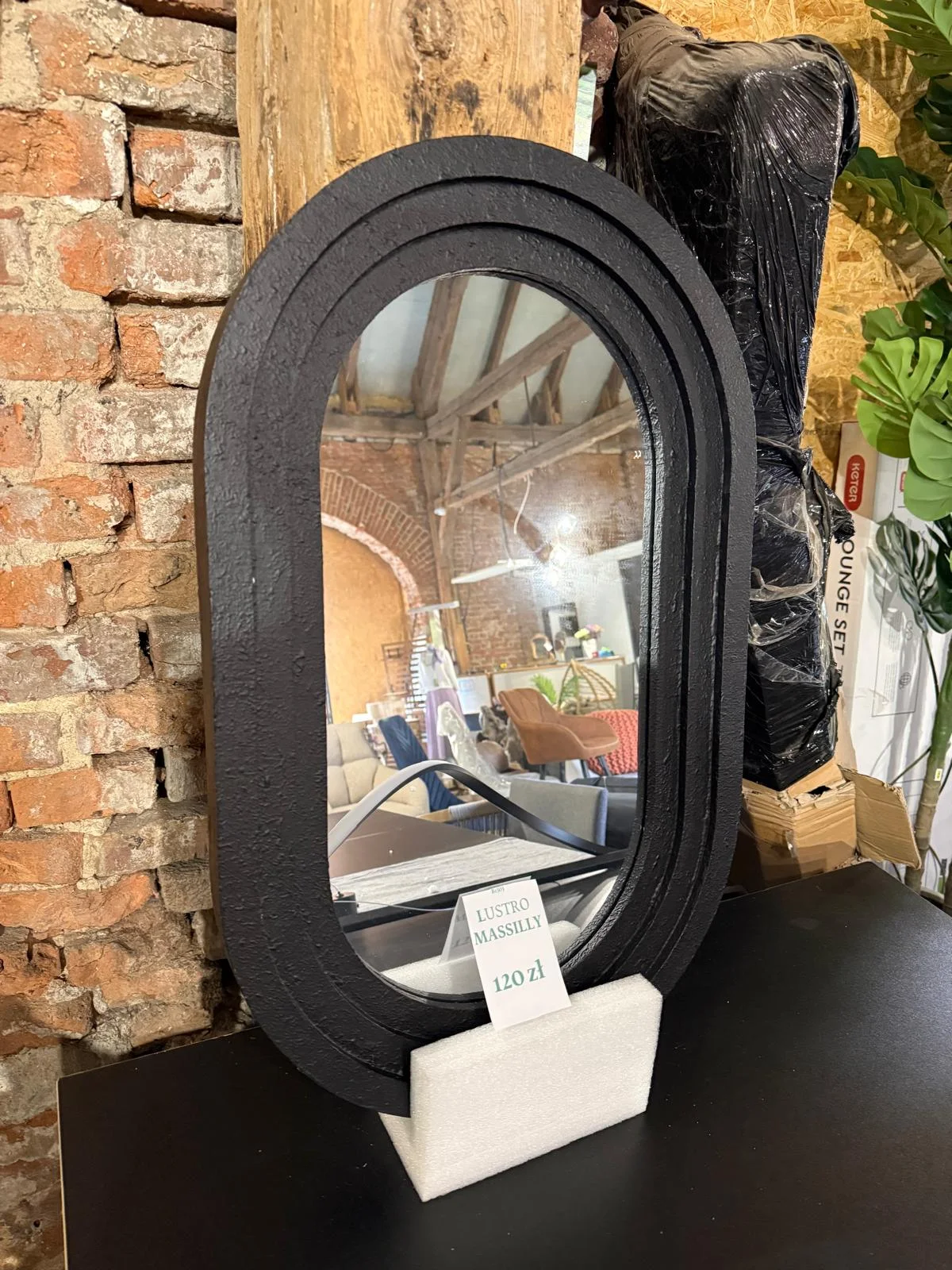 Czarne lustro ścienne MASSILLY 43 × 69 cm z dekoracyjną zaokrągloną ramą, dostępne w Home & Garden Outlet pod Wrocławiem.