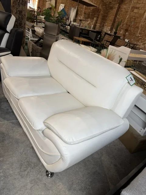 Biała sofa 2-osobowa LEIRA tapicerowana ekoskórą, z szerokimi podłokietnikami i srebrnymi metalowymi nóżkami, dostępna w Home & Garden Outlet pod Wrocławiem.