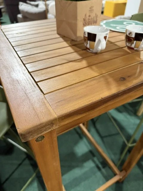 Brązowy stolik barowy z drewna akacjowego z listwowym blatem, idealny na taras, balkon, patio lub do ogrodu, dostępny w Home & Garden Outlet pod Wrocławiem.