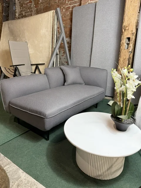 Ciemnoszary szezlong prawostronny CHEVANNES obity tkaniną boucle, z poduszką dekoracyjną i smukłymi metalowymi nóżkami, dostępny w Home & Garden Outlet pod Wrocławiem.